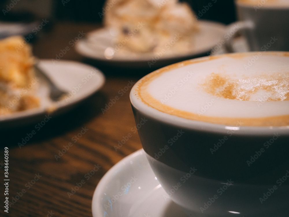 Cup of coffee with milk and cake in background Cup of coffee with milk and cake in background