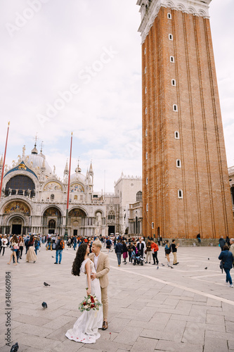 Wedding in Venice, Italy. The bride and groom are hugging in Piazza San Marco, overlooking Campanila and St. Mark Cathedral, among a crowd of tourists. photo