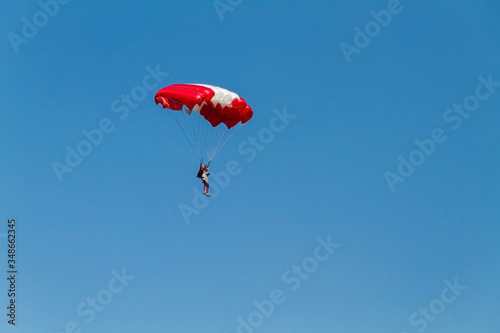 the sportsman lands to the ground with a red and white parachute.