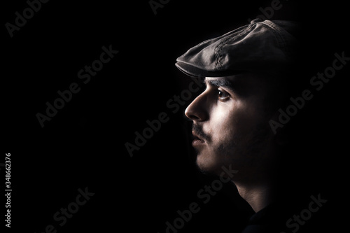 Portrait of cute young guy with moustache and a hat on black, dark background.