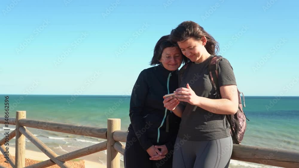 Successful, happy middle-aged woman with a young girl, on a rock near the ocean laughs from what he saw on the phone. Portugal. Vilamoura. Mother with daughter. Successful, happy middle-aged woman with a young girl, on a rock near the ocean laughs from what he saw on the phone. Portugal. Vilamoura. Mother with daughter.