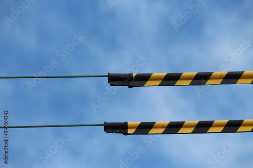 Yellow and black striped synthetic tubes that (Tiger tails) They are clipped together over powerlines to provide a useful visual indication of live overhead powerlines. Blue sky photo