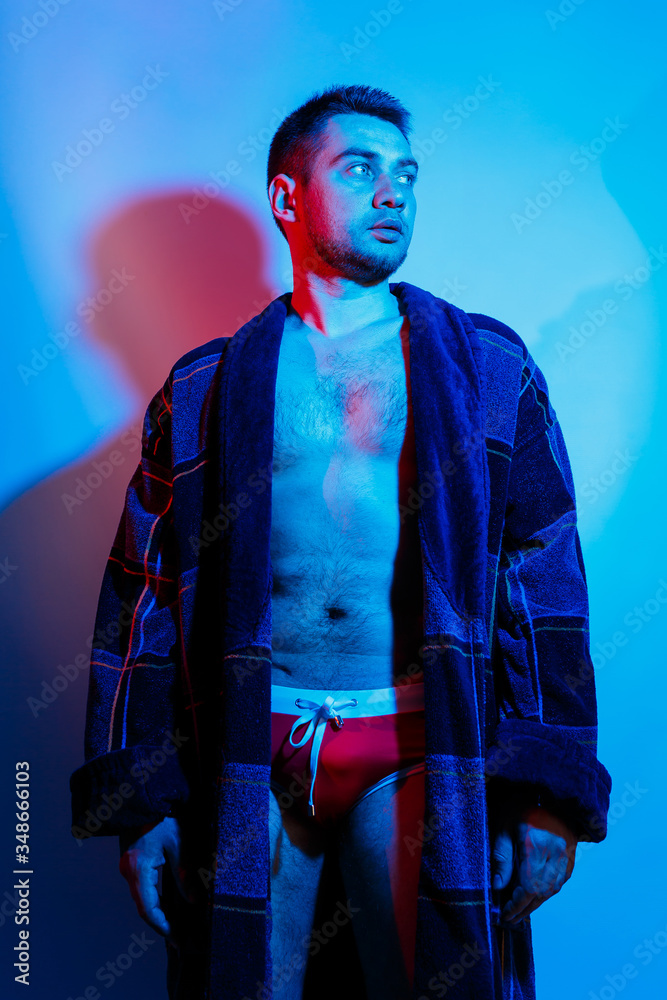 A man in a bathrobe and underwear. Studio lighting red and blue on a male body. Outrageous guy model