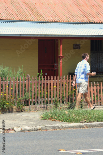 Old colonial house with iron roof and picket fence in the Inner West. Also man walking past with a takeaway coffee.  photo