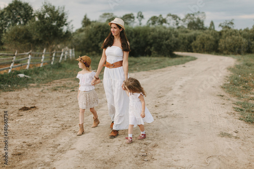 Mom with 2 daughters walks the village in white dresses on a summer day, life on the farm