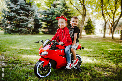 Children riding on the red toy motorcycle in the summer park