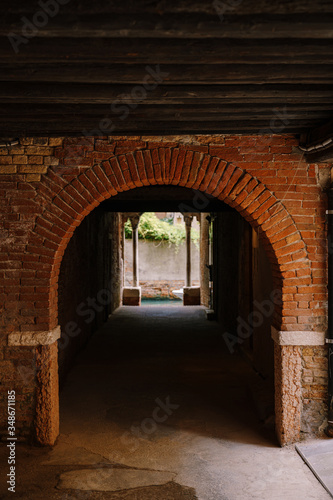 View from the building on to a small narrow canal between houses in Venice  Italy. A view from a tunnel with brick walls  two antique columns and water in the sea.