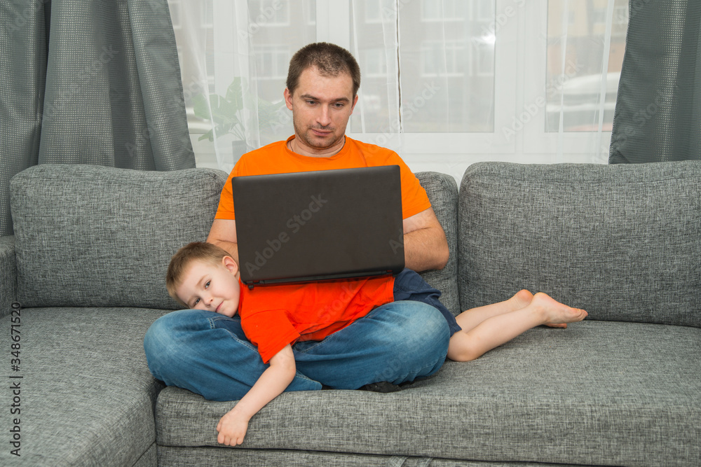 Man in orange shirt tries to work on laptop during his son disturb him. Home office work and stay home concept Man in orange shirt tries to work on laptop during his son disturb him. Home office work and stay home concept