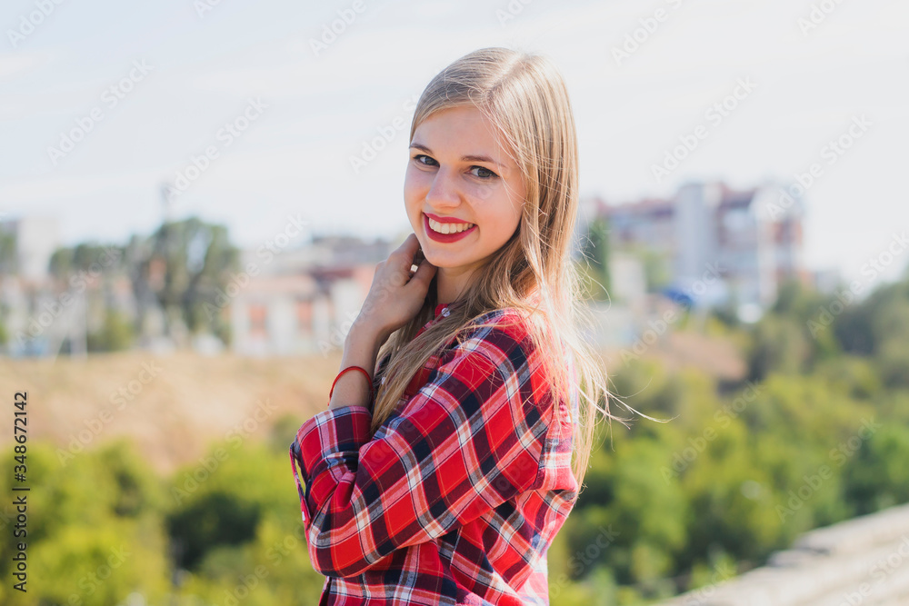 young blonde girl in a red shirt on the roof of the building looks at the camera