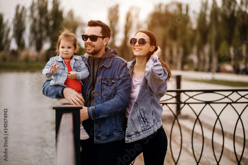 family walk, father and mother hold daughter in their arms, sunset, mom straightens her hair photo