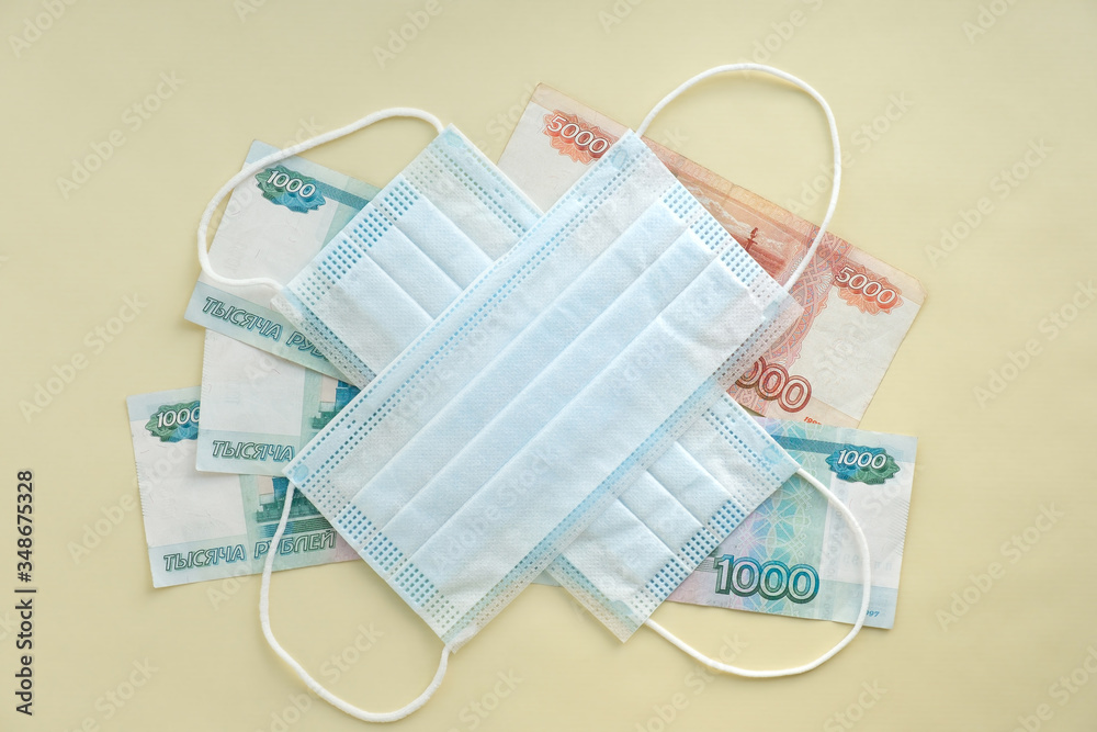 concept, the epidemic put an end to the Russian economy. two blue medical masks lie in a cross on top of one thousand and five thousand Russian rubles banknotes. the view from the top. concept, the epidemic put an end to the Russian economy. two blue medical masks lie in a cross on top of one thousand and five thousand Russian rubles banknotes. the view from the top.