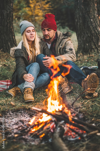 Traveler couple camping in the forest and relaxing near campfire after a hard day. Concept of trekking, adventure and seasonal vacation.