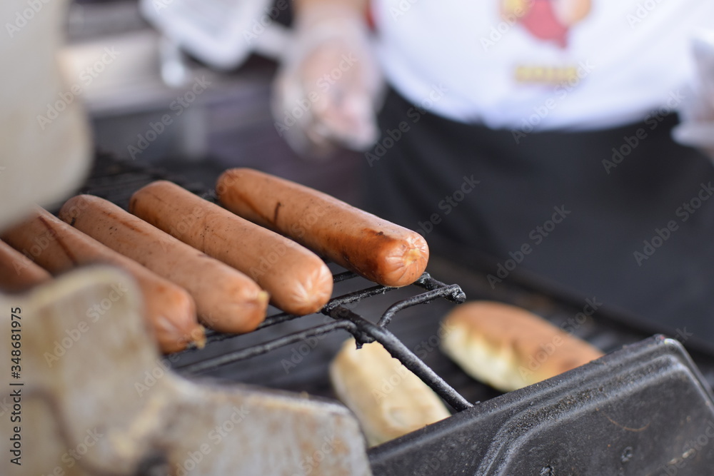 Five sausages on a grill cooking to eat them in hot dogs.