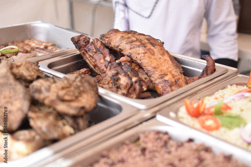 Different food trays of a restaurant, where you see different types of meat including ribs, sausages and rice.