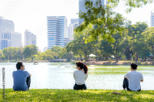 Asian young three man and woman talking and relaxing with they friend and wearing mask sitting distance of 6 feet distance protect from COVID-19 viruses for social distancing in park. photo