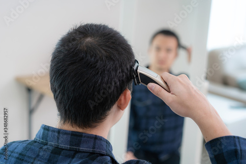 Asian man cutting own his hair with haircutting scissors at home they stay at home and shelter In place during time of home isolation against Novel coronavirus or COVID-19