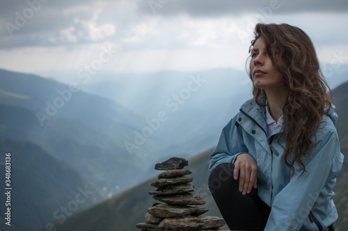 Adventurous girl siting on the edge of a cliff overlooking the beautiful . Beauty girl resting after jogging on the mountain road on the sunset with beautiful landscape view. The top of the mountain