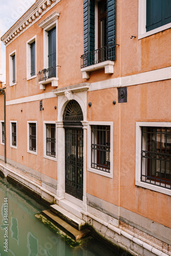 Close-ups of building facades in Venice, Italy. A two-story building near the water in a narrow Venetian canal. On the ground floor there are forged metal bars on the windows and doors © Nadtochiy