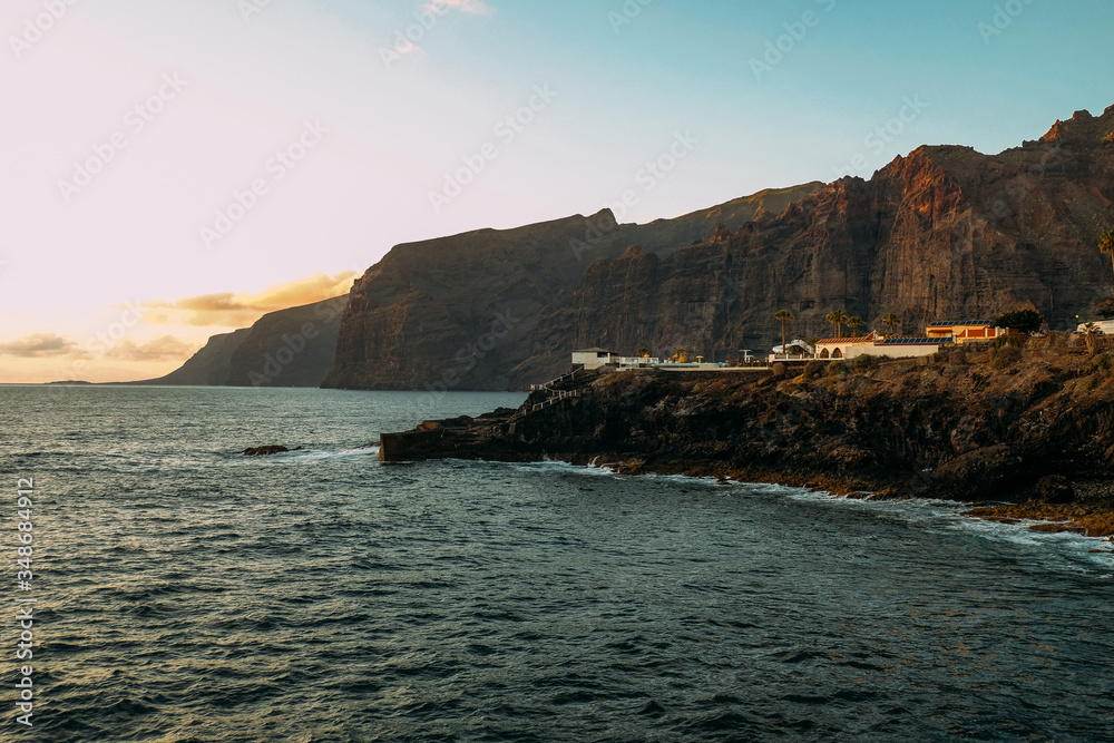 Sunset over the ocean on a tropical island. City in the mountains and ocean at sunset Sunny evening on Tenerife. Pink ocean waves. Background color with gradient and grain, sound effect. los gigantes