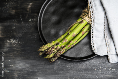 Bunch of fresh asparagus on a black plate on a wooden table. Photo taken with selective focus.