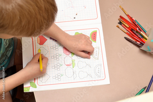 Home schooling during the worldwide outbreak of coronavirus. The child draws around a dotted line drawings. The early development of the child. photo