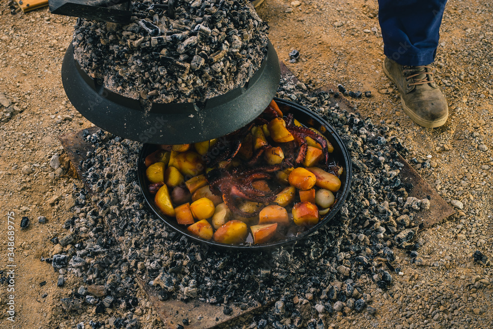 Cooking traditional balkan turkish bosnian dalmatian meal Peka in metal  pots called sac sach or sache. Detail of squid or octopus with potatoes  under Sache. Sac is covered with hot charcoal. Stock