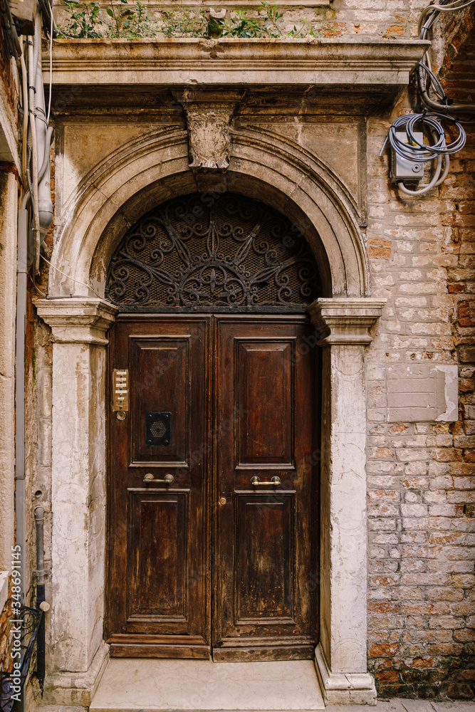 Close-ups of building facades in Venice, Italy. An old, gloomy wooden door, brown. Stone arched doorway. The facade of a brick house with hanging electrical wires.