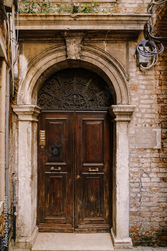 Close-ups of building facades in Venice  Italy. An old  gloomy wooden door  brown. Stone arched doorway. The facade of a brick house with hanging electrical wires.