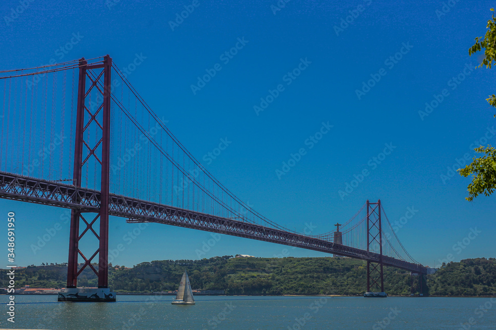 Ponte de 25. april in Lisbon, portugal, taken on a sunny day. A small sailboat is just passing under the bridge.