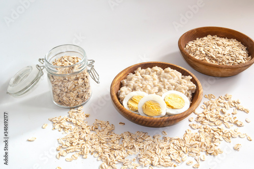 cooked oatmeal porridge in a wooden bowl on a white background with a boiled egg