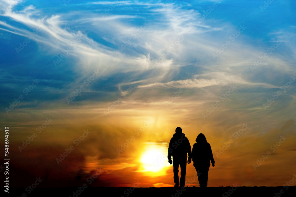 Silhouette of man and woman holding hands and walking together towards spectacular sunset