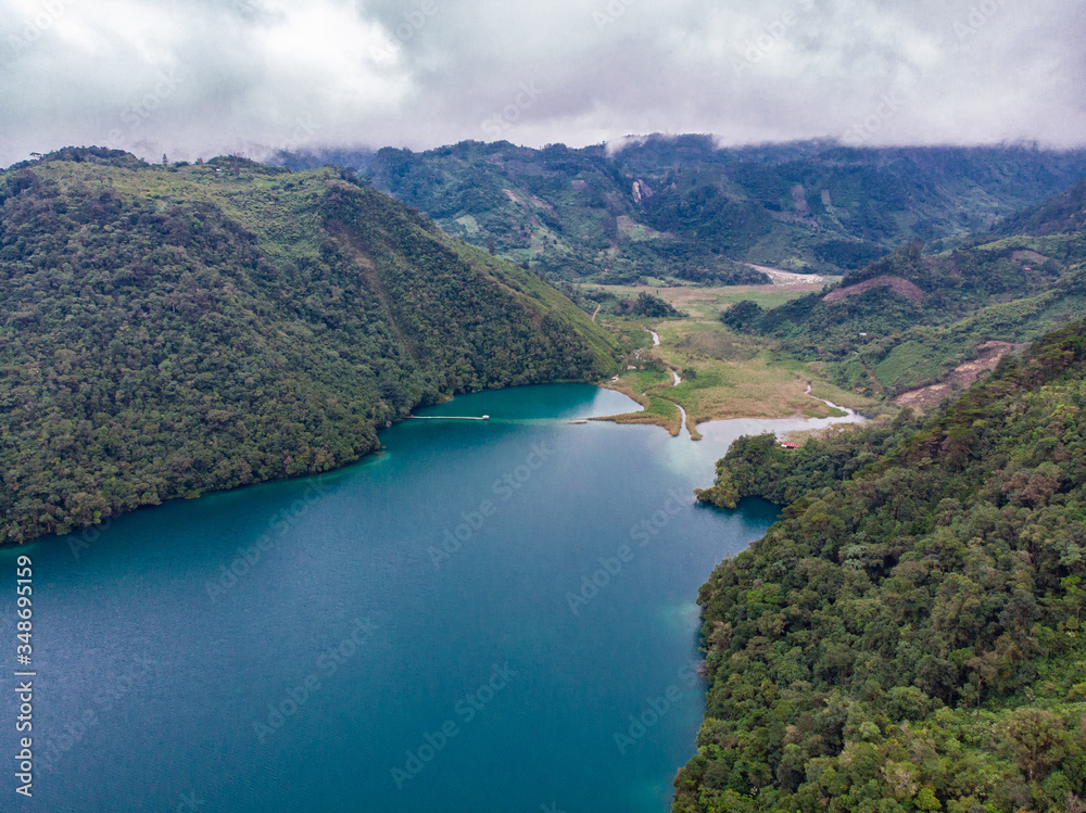 Aerial view of the Laguna Brava in Guatemala, on a cloudy day where you can see its turquoise water and the beautiful mountains that surround the lake.