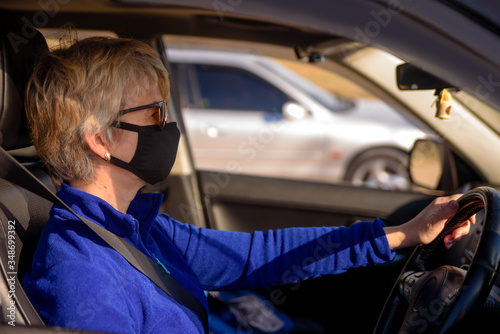 Woman in black face mask and sunglasses is driving a car and looks at the road. Left-hand drive. Coronavirus infection control concept.