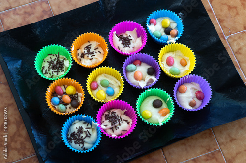 Obraz na płótnie Delicious cakes cooked at home. Homemade cupcakes in multi-colored silicone molds and with colored chocolates inside on a baking tray. w salonie