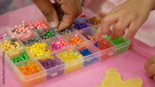 Hands of little baby girls, sisters, and their mother learning to play with colorful beads at home - Beading with Your Children