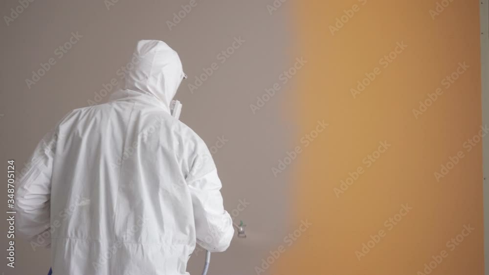 Worker painting the orange wall by airless spray gun with white color