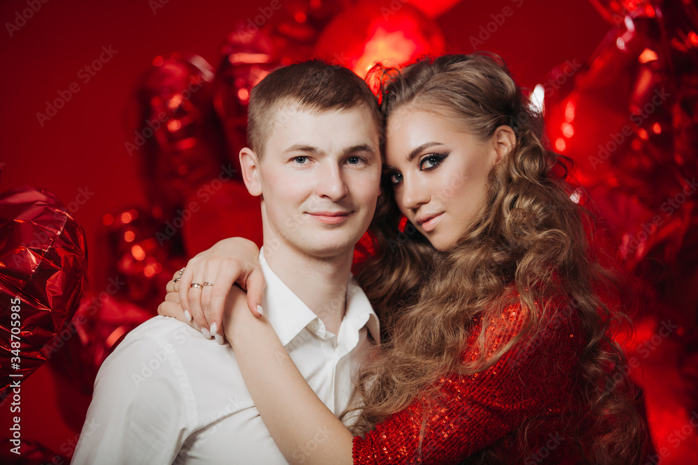 Loving couple with red balloons hearts. Man and woman celebrate valentine's day. Romantic date on a red background. Boyfriend and girl have fun on holiday.