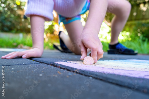 Young caucasian girl drawing rainbow with chalk on floor with shallow focus