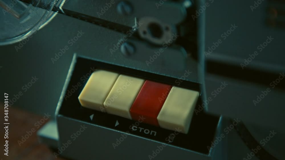 Male hand presses red stop button on retro movie projector to switch the projector off, testing old technology before watching old movie, the film reel stops rotating, light is fading, Slow motion.