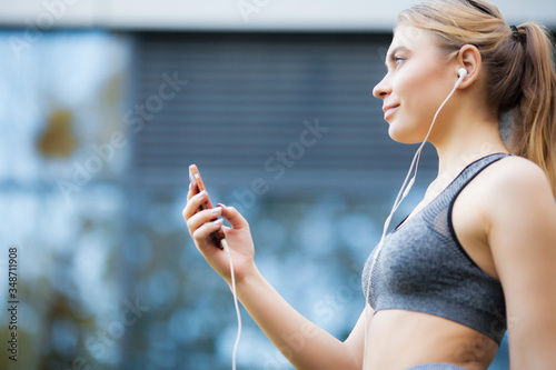 Pretty woman doing fitness outdoors listening to music