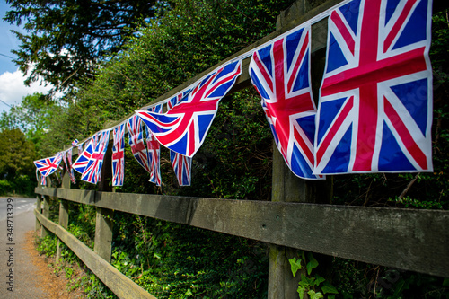 Union Jack bunting on a fence row, many flags in row on a string, front of garden VE day decorations in UK, memorial symbol of winning second world war, flags blowing on wind