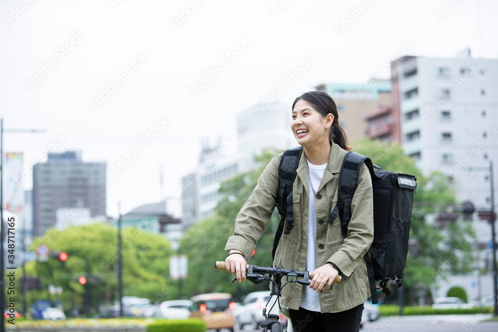 自転車で荷物の配送を行う若い女性 自転車で荷物の配送を行う若い女性