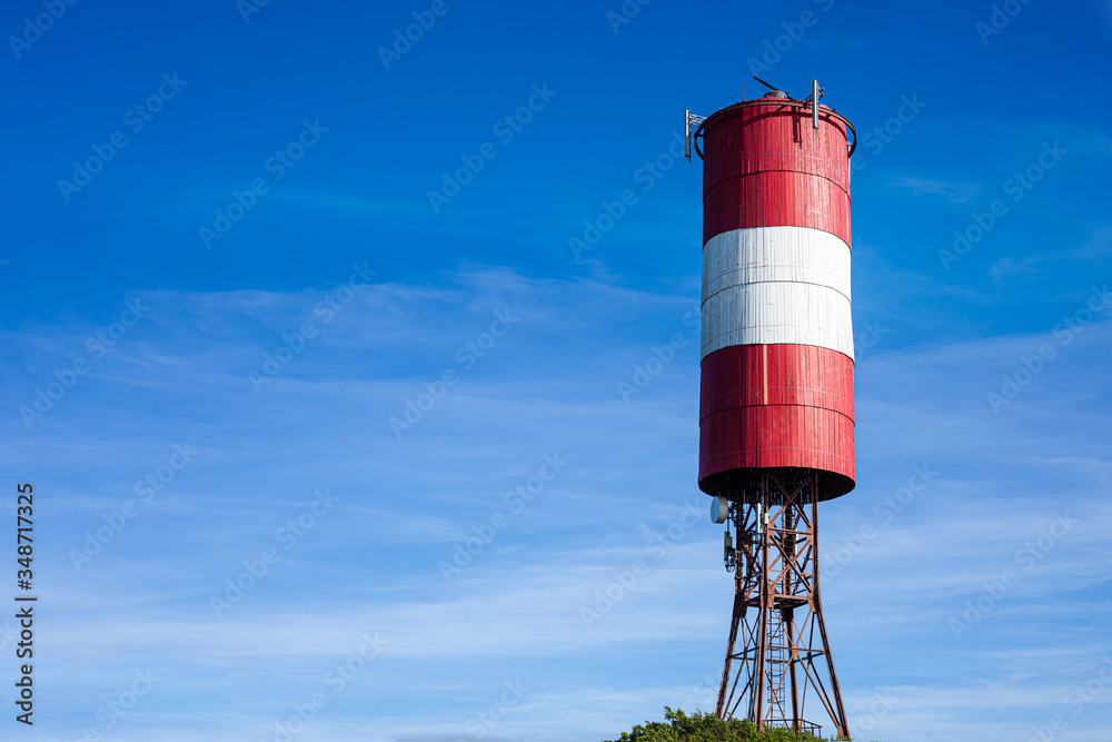 Red and white striped water tower against blue sky. 