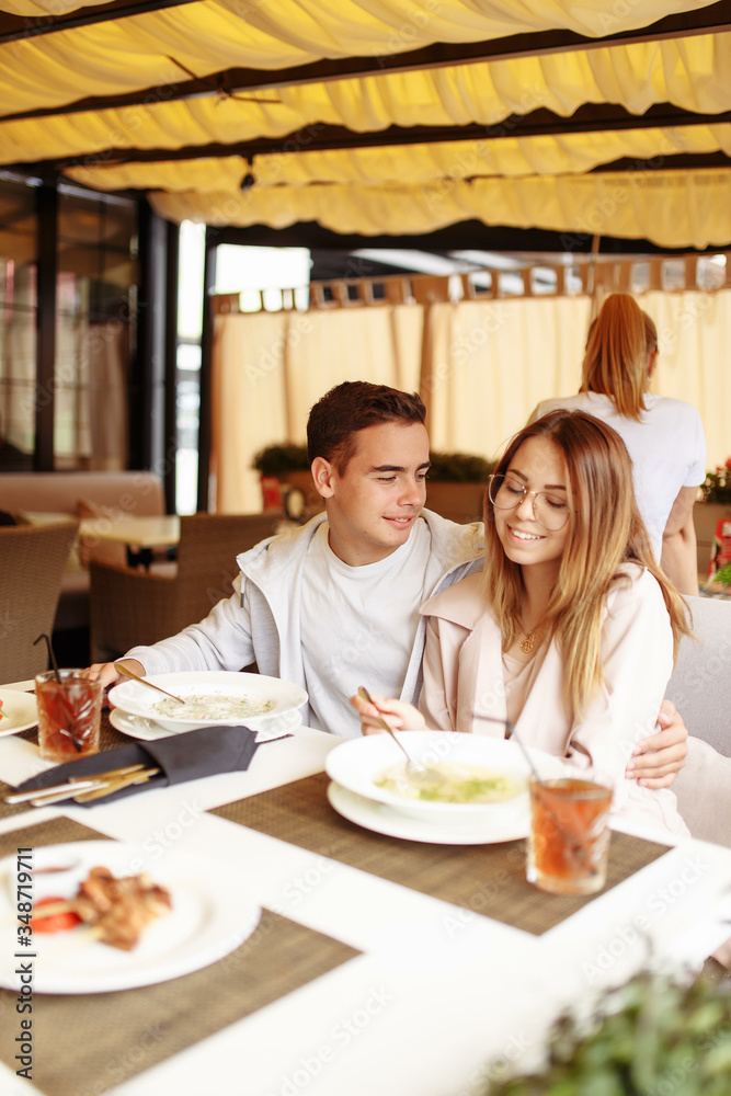 A cheerful and beautiful couple are relaxing on a summer terrace in a restaurant with food and drinks. The guy and the girl have fun on the terrace