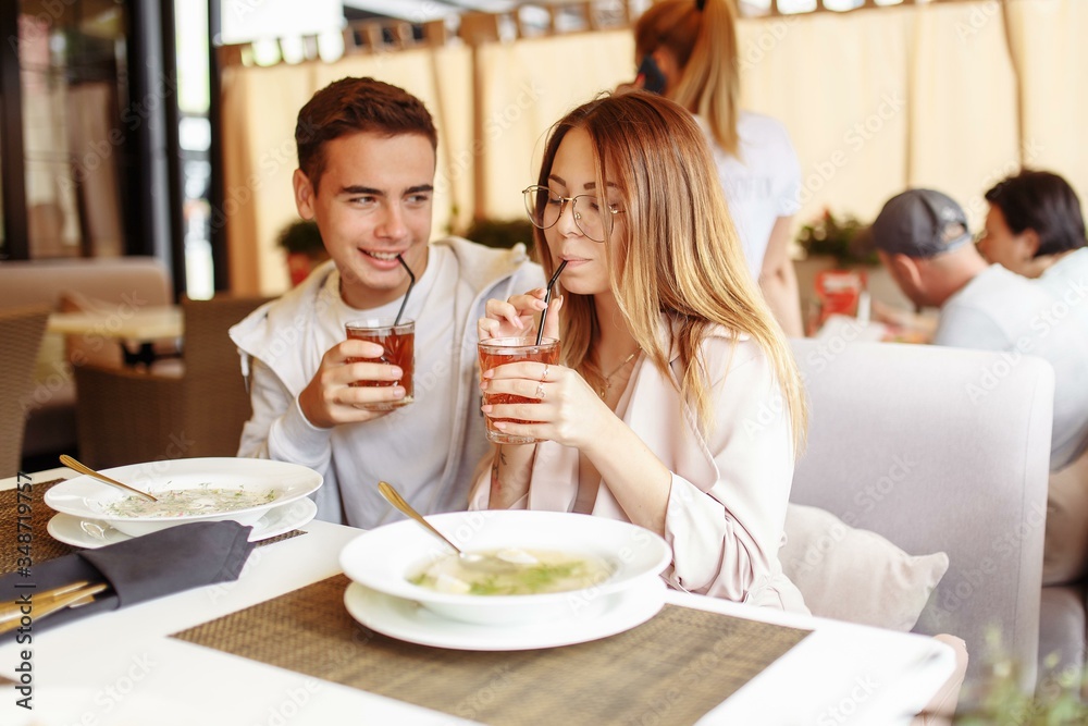 A cheerful and beautiful couple are relaxing on a summer terrace in a restaurant with food and drinks. The guy and the girl have fun on the terrace A cheerful and beautiful couple are relaxing on a summer terrace in a restaurant with food and drinks. The guy and the girl have fun on the terrace