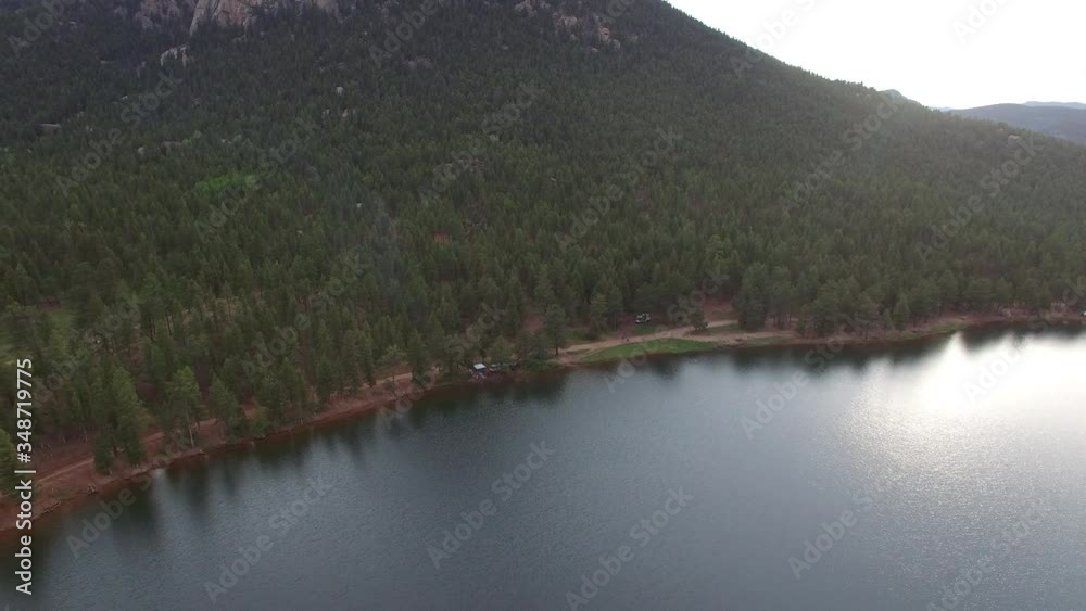 Aerial shot of campsite at calm lakeshore near green forest, drone ascending over beautiful lake by mountain during sunset - Lake Wellington, Colorado Aerial shot of campsite at calm lakeshore near green forest, drone ascending over beautiful lake by mountain during sunset - Lake Wellington, Colorado