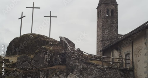 Camera tilts up towards a small rock church with three crosses alongside, in a wood of the Italian Alps 4k slow motion bell tower detail. photo