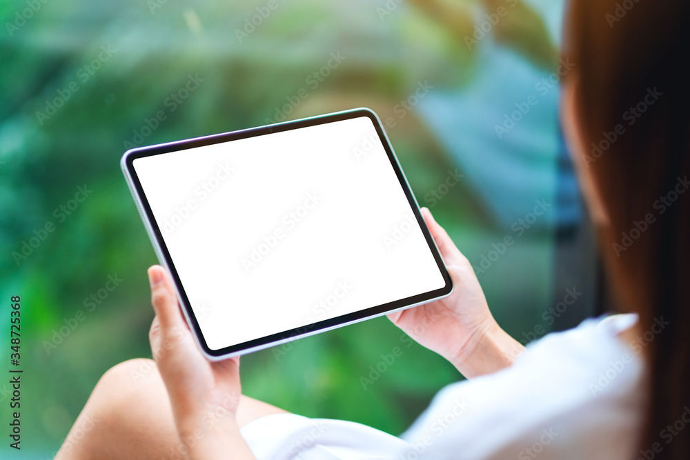 Mockup image of a woman holding black tablet pc with blank white desktop screen , green nature background Mockup image of a woman holding black tablet pc with blank white desktop screen , green nature background