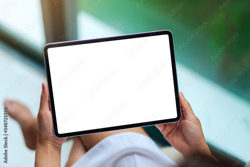 Mockup image of a woman holding black tablet pc with blank white desktop screen , green nature background