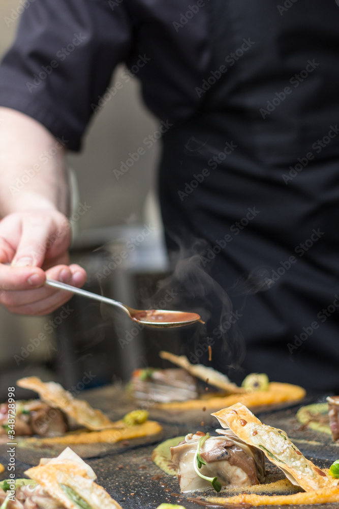 Chef in black outfit pouring sauce on food